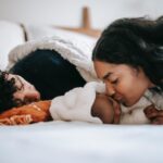 Parent kissing sleeping baby while second parent is also asleep.