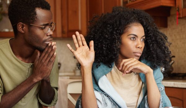 People, relationships problems and divorce. Repentant worried dark-skinned male keeping hands pressed together, begging offended wife to forgive his infidelity, mad woman not looking at him at all